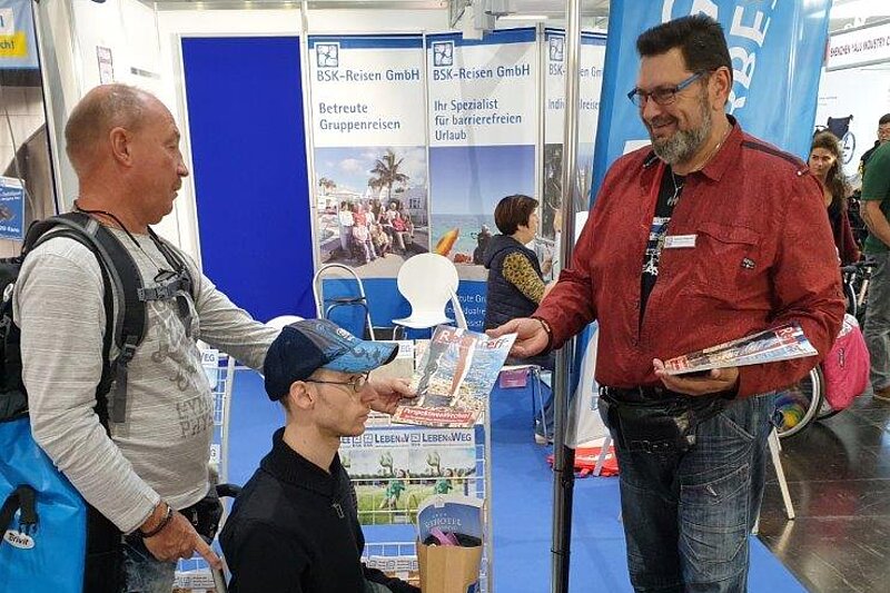 Zwei Menschen, einer davon im Rollstuhl, werden bei einer Messe von einem BSK-Mitarbeiter beraten.